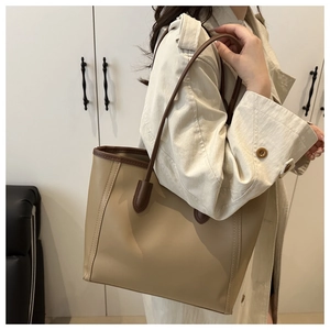 Side view of large khaki tote bag with dark brown trim worn on person in lifestyle setting