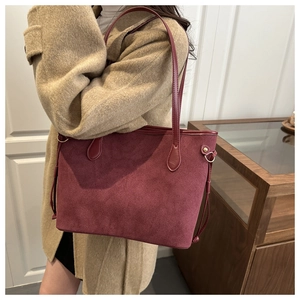 Borsa tote in camoscio rosso scuro con manici in pelle indossata a spalla da una modella