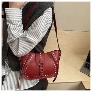 Close-up of red leather shoulder bag with metallic silver rivets and buckle flap detail