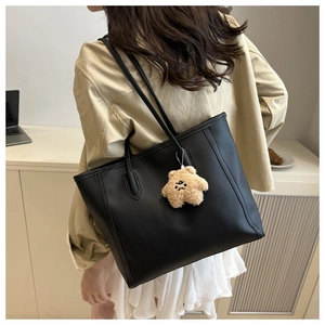 Close-up of black matte leather tote bag with a brown plush star charm on a long shoulder strap