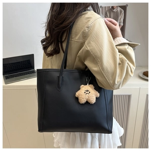 Detail of a black large tote bag with bear charm shown on model in a modern office setting
