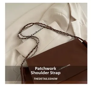 Detail view of the brown leather shoulder bag featuring a metal chain strap and logo
