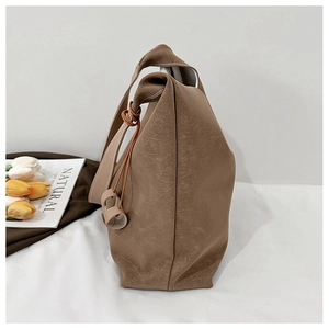 Detail of tan tote bag featuring knotted strap design and rustic faux leather texture