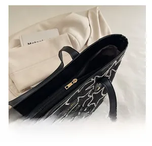 Macro view of black tote bag showing smooth gold zipper and white star embroidery detail