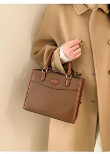 Dettaglio di una borsa bicolore marrone con finiture dorate abbinata a un cappotto beige