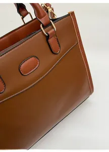 Dettaglio della borsa tote in pelle marrone con cuciture chiare e finiture dorate