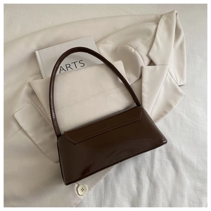 Détail du sac baguette marron foncé brillant sur un blazer crème en similicuir lisse