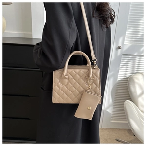 Detail of beige quilted shoulder bag with top handles and a matching coin purse charm