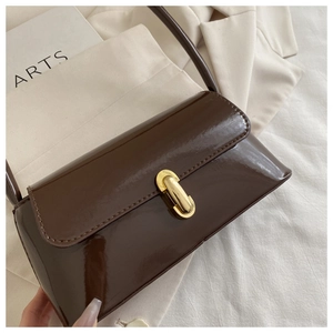 Détail d'un sac d'épaule en cuir verni marron brillant avec fermoir doré en métal ovale