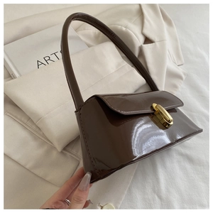 Détail du sac sous l'aisselle en cuir verni marron foncé avec fermoir doré et fini brillant