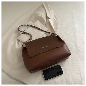 Detail of brown faux leather shoulder bag with metal chain strap and minimalist text