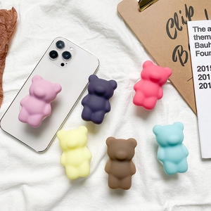 Flat lay of colorful matte bear phone grips in pink, purple, and blue on rustic background