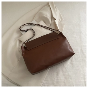 Detail of a dark brown leather tote bag with metal chain strap on a white blazer background