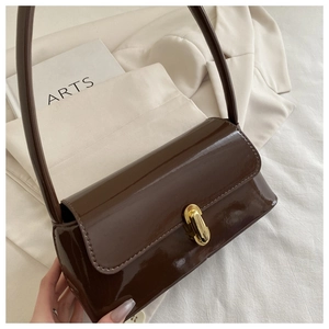 Détail d'un sac à main marron foncé brillant avec fermoir doré sur fond minimaliste