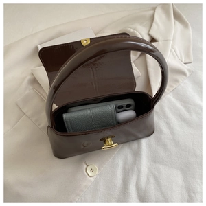 Intérieur du sac en cuir verni marron foncé montrant l'espace de rangement et fermoir doré