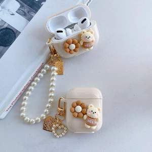 Detail of cream AirPods case with 3D bear, floral decor, and pearl lanyard on white desk
