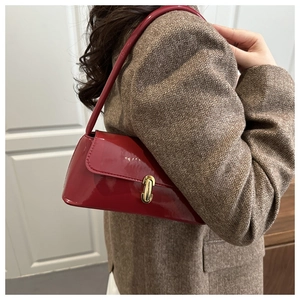 Détail du sac d'épaule en cuir verni rouge avec boucle dorée sur un blazer marron