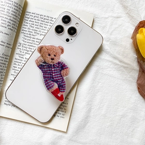 Close-up of cute teddy bear acrylic griptok attached to a white phone over a book
