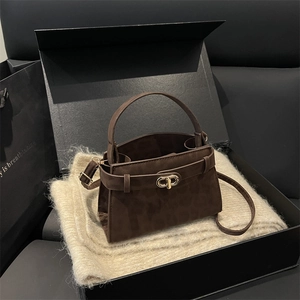 Deep brown matte suede handbag with gold lock on beige fabric inside a gift box