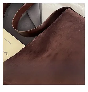 Detail shot of the dark brown matte suede texture and smooth leather strap of the tote bag