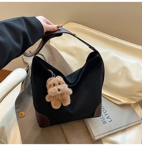 Detail of large black tote bag with brown leather corners and a plush dog charm