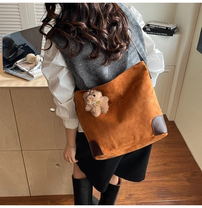 Detail of brown suede tote bag with leather corner reinforcement and cute bear charm