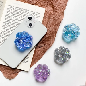 Detail showing glittery resin cat paw phone grips in blue and purple on a white smartphone