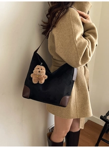 Detail view of large black and brown tote bag with plush bear charm on a female model