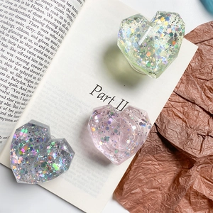 Detail of three heart-shaped resin phone grips with glitter sequins on an open book