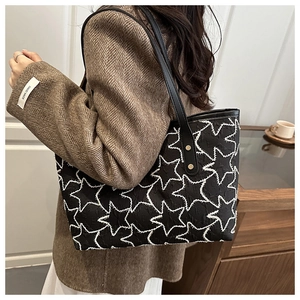 Detail of black tote bag featuring white stitched star patterns and textured fabric