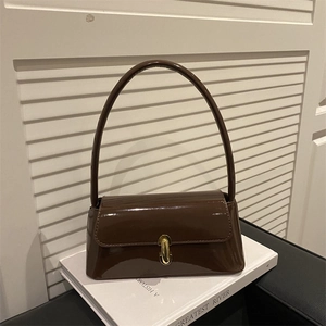 Sac baguette en cuir verni marron brillant avec boucle dorée sur fond de livre blanc