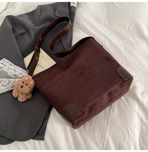 Detail of dark brown suede tote bag with leather strap and plush dog charm in retro style