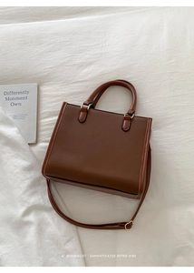 Vue détaillée du sac à main vintage marron foncé avec doubles anses sur fond de tissu blanc