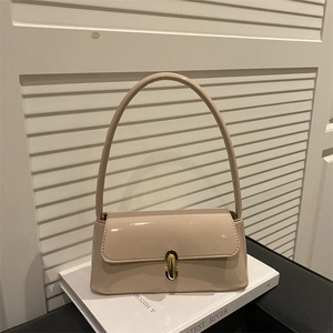 Sac à épaule élégant en cuir verni beige avec fermoir doré posé sur un livre