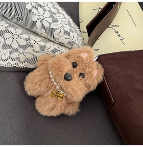 Plush brown dog charm with pearl necklace and gold bone tag on a suede tote bag