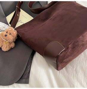 Detail of a dark brown suede tote bag with plush puppy pendant on textured fabric