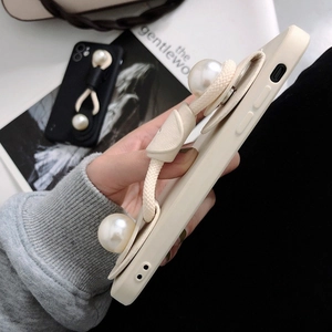 Close-up of cream iPhone case with pearl wrist strap and woven handle on magazine