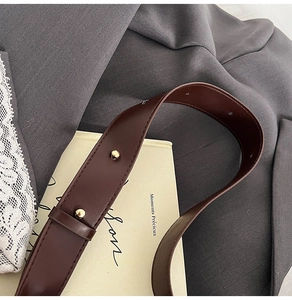 Detail of dark brown leather strap with golden rivets and stitching on a tote bag