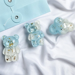 Detailed close-up of blue resin bear and cloud phone grips with embedded gold foil flakes