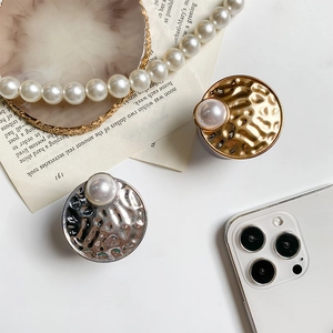 Close-up of gold and silver phone grips with hammered metal texture and large white pearl