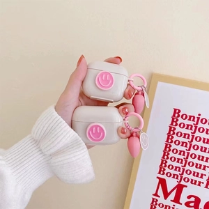 Detail of white AirPods cases with pink smiley patches and heart charms held by a model