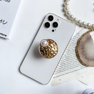 Detail of a gold metallic phone grip with textured hammer patterns and a large pearl inlay