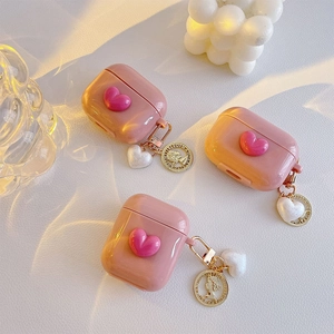Pink heart AirPods case with gold coin and heart charms on a textured background
