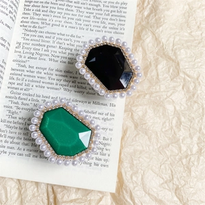 Vintage style brooches with emerald and black gems surrounded by pearls on an open book