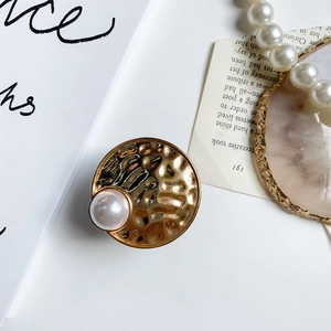 Macro detail of a vintage gold hammered metal phone grip featuring a large white pearl accent