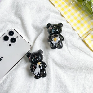 Detail of two black glitter bear phone grips with astronaut miniature on a white cloth