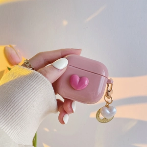 Pink heart AirPods case with pearl keychain shown in a hand with a warm sunset vibe
