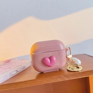 Pink silicone heart case for AirPods Pro with golden keychain and pearl on a wooden desk