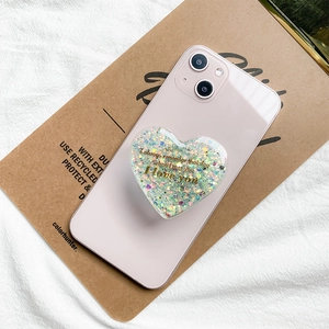 Glittery heart-shaped phone grip with golden text on pink smartphone