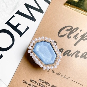 Macro detail of foldable phone grip featuring blue resin center with pearls and rhinestones